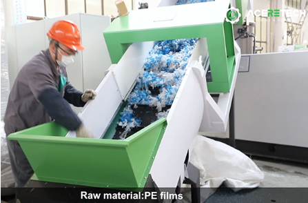 作業員がPEフィルム（ラップや包装フィルムなど）廃材を大型の投入ホッパーに投入しています。 ここから全自動リサイクルの工程がスタートします。